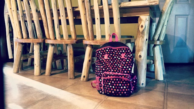 Black backpack with a pink outline and shapes leaned on a wooden chair at the table