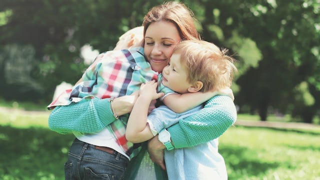 A mother holding her two kids while smiling in nature during a sunny day