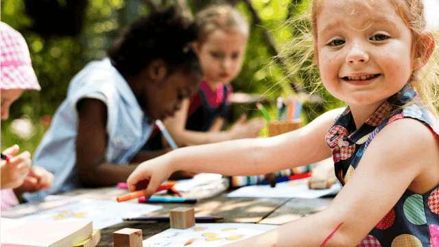 Four children sitting at a backyard bench in a Kindergarten and drawing pictures