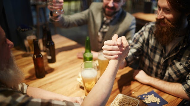 A group of guys sitting at a table with beers on it, having fun and arm wrestling, the rock test
