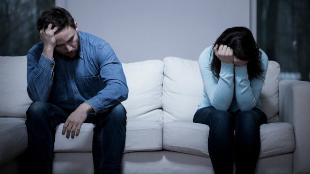 A wife and a husband sitting together at a couch after a verbal fight