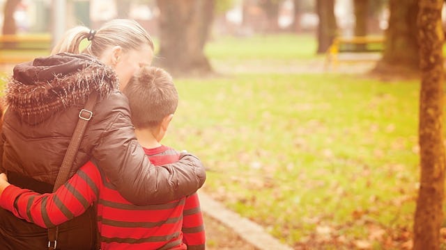 A mother hugging her son in a striped shirt while walking through the park after leaving her narciss...