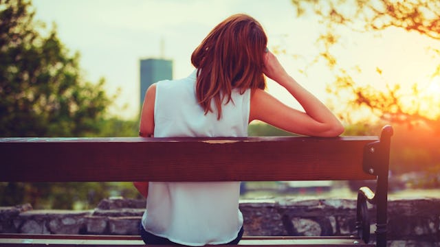 A girl suffering from mental illness sitting alone on a bench looking at the sunset