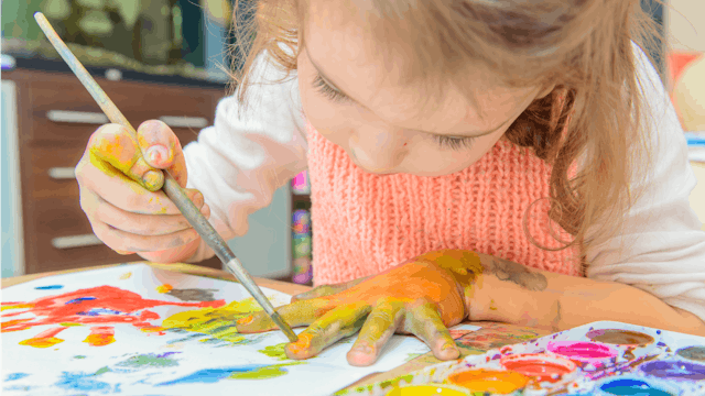 A small girl drawing her hands with a brush and watercolors