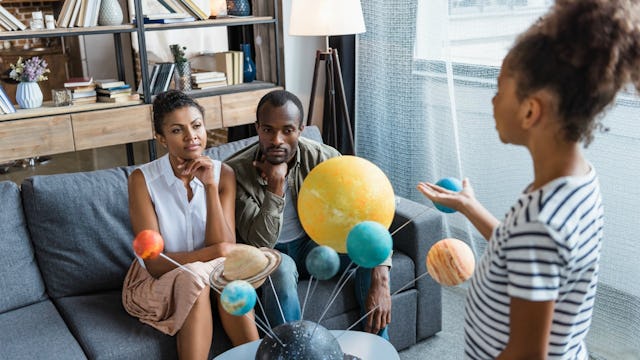 Parents learning geography with their daughter with a sculpture of solar system planets hanging in w...