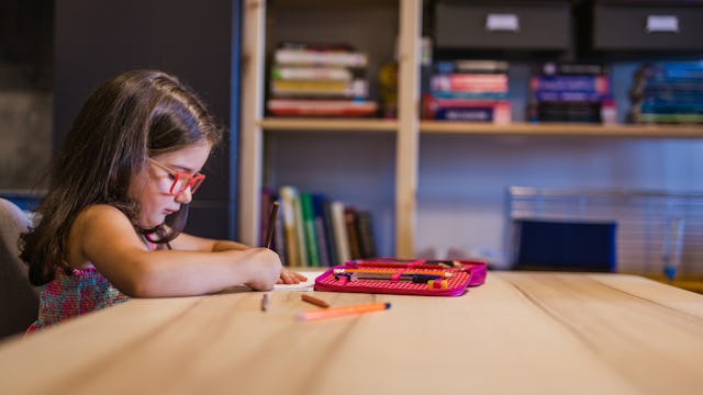 Little girl with red glasses sitting at a table, playing with coloring