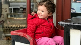 Smiling little girl with brown short hair wearing a red jacket and pink pants while sitting