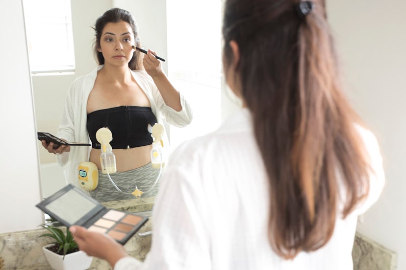 A young mother doing makeup in front of the mirror while doing a hands-free pumping 