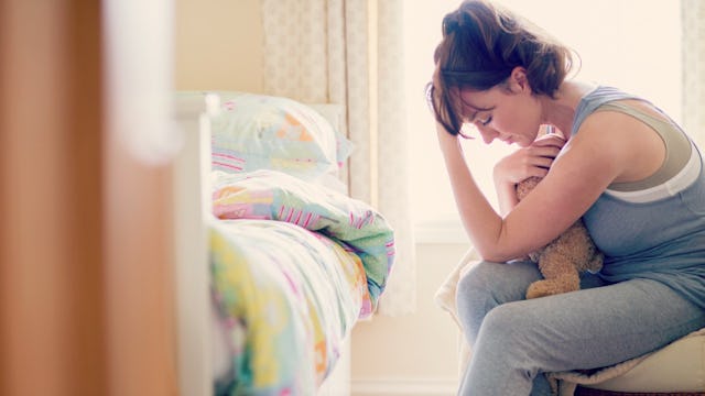A woman sitting and hugging a teddy bear while looking disappointed