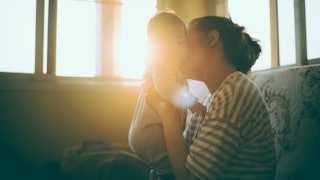 A woman experiencing postpartum panic attacks holding a baby with sunlight shining through the windo...