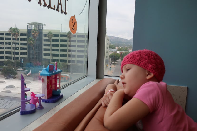 Little girl with cancer looking out the window of her hospital room