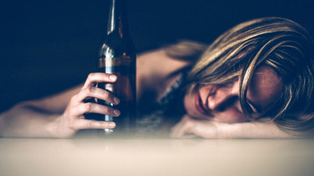 A young blonde girl drunkenly lying with her hair on the table, feeling the shame of alcoholism.