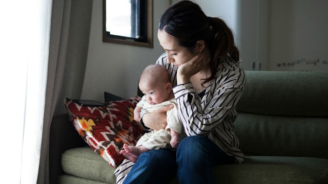 A mom in a black and white striped shirt is sitting on a grey sofa with her baby