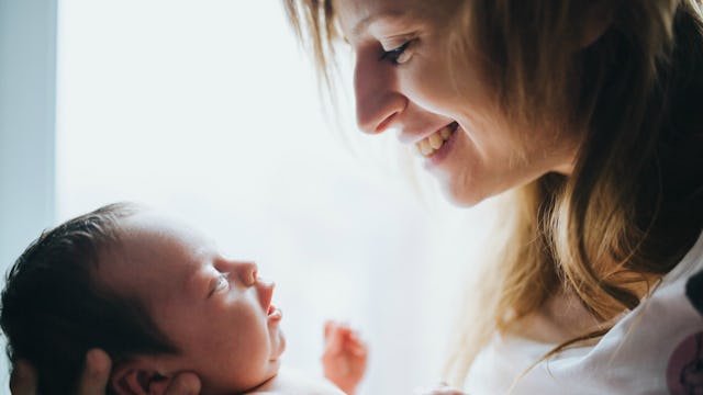 A new mom in a white shirt laughing while she is holding and looking at her newborn baby