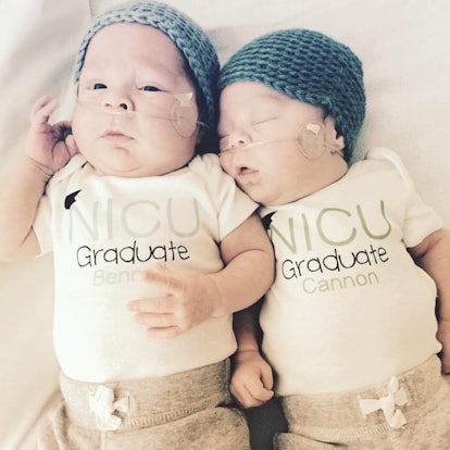 Pale twins wearing blue wool hats and white shirts reading "NICU graduate," one of them sleeping