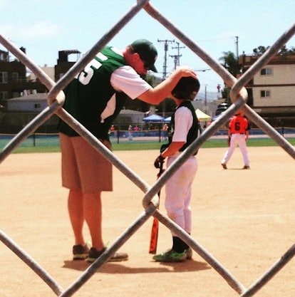 Child and his baseball coach on a baseball field. The coach is patting the child on his helmet, ackn...