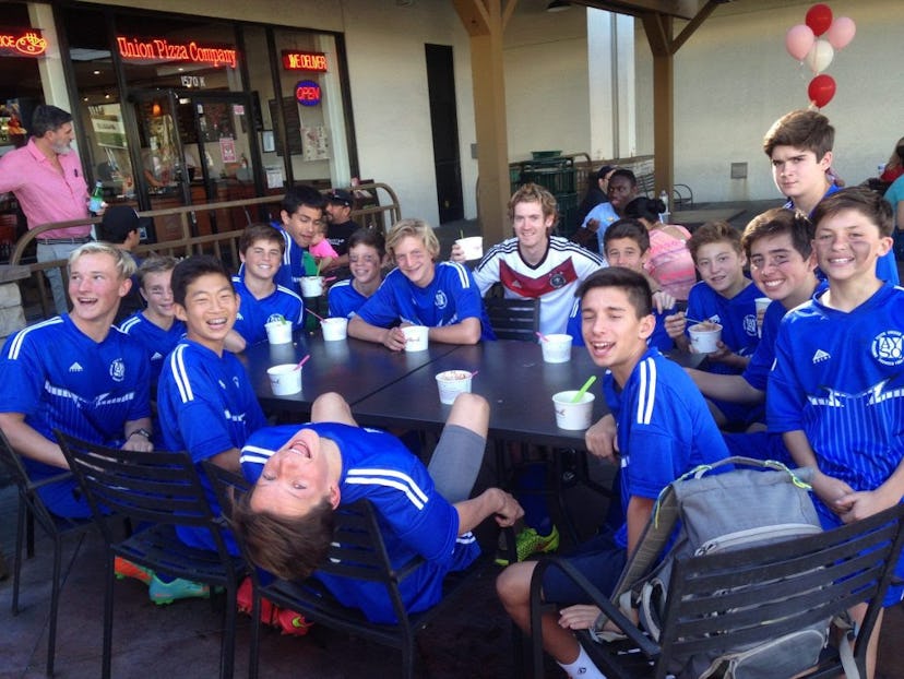 Soccer team consisting of 14 boys and their coach sat at restaurant table outside eating ice-cream. ...