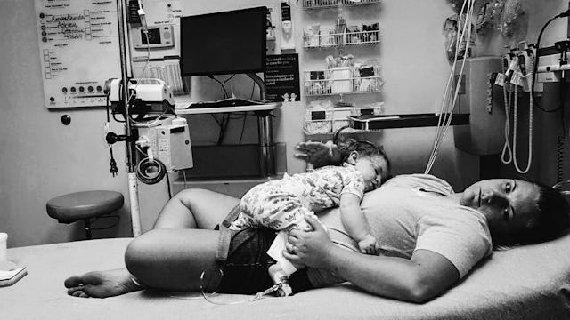 A 'medical mama' lying down in a hospital bed, holding her sick child on her belly.