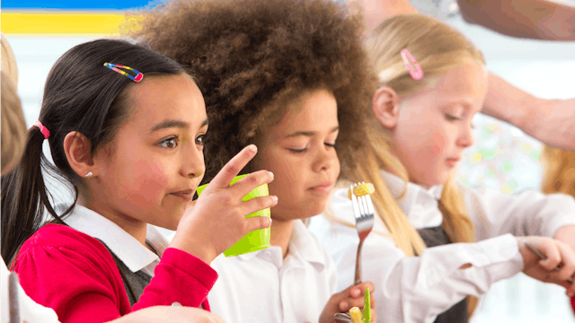 A curly-haired girl checking if she can eat a school meal due to her allergy.
