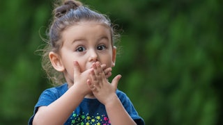 3-year-old girl holding her hands over her mouth with a surprised expression on her face