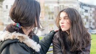 Two girls with concerned facial expressions sitting on a bench, talking about mental health issues.