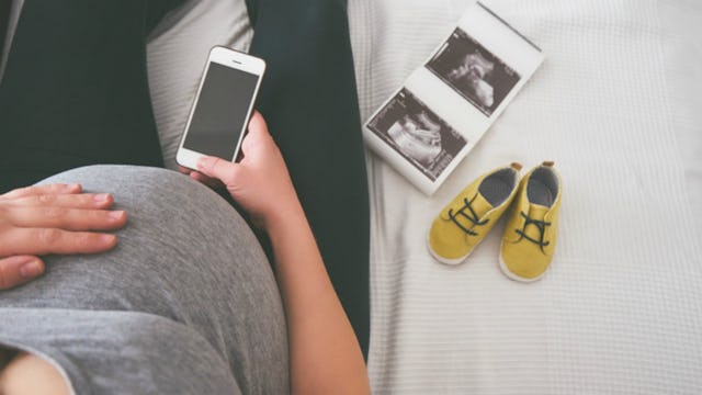 Pregnant lady sitting and scrolling her phone while expecting