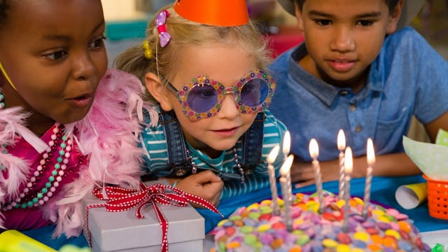 A girl sitting between her two friends and about to blow out the candles on her birthday cake at her...
