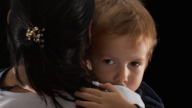 A boy with an invisible disability being held by his mother and looking over her shoulder