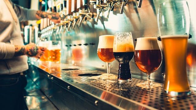 A man pouring his beer in the background of four poured glasses on a beer dispensing device.