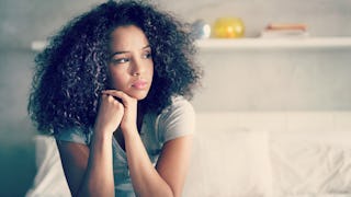 A young woman who recently experienced a miscarriage with a sad facial expression sitting on a white...