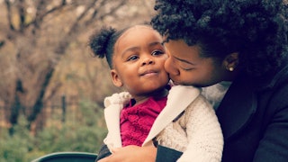 Mom gives her daughter a kiss in a cheek while she sits her in her lap.