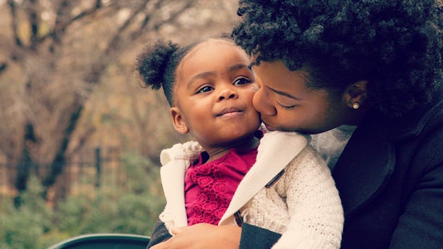 Mom gives her daughter a kiss in a cheek while she sits her in her lap