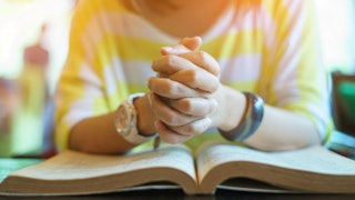 The hands of a woman victimized by the Purity Movement in a yellow-white striped sweater praying abo...