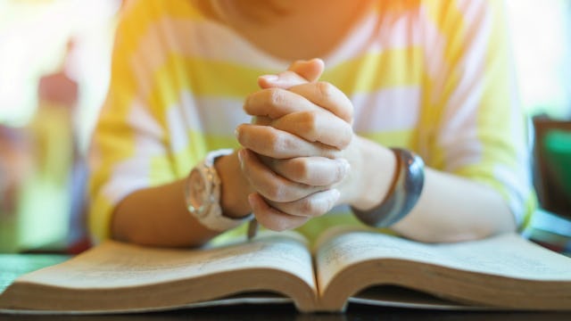 A woman victimized by the Purity Movement in a yellow-white striped sweater praying above the Bible