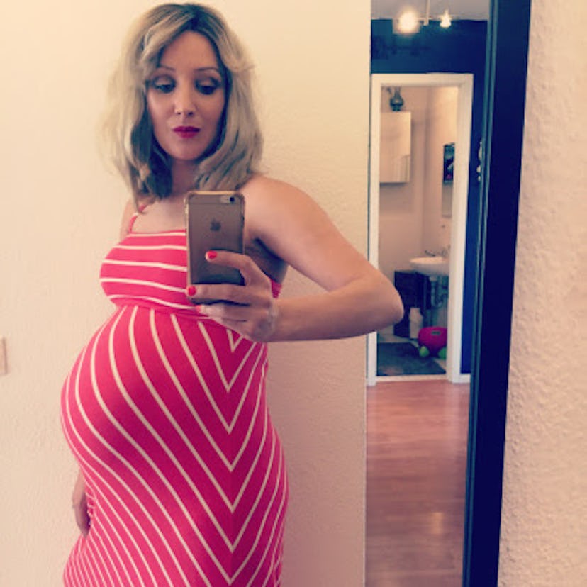 Pregnant woman taking a mirror selfie in a pink dress with white stripes
