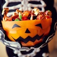 A child in a Halloween costume holding candies in the pumpkin bowl 