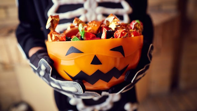 A child in a Halloween costume holding candies in the pumpkin bowl