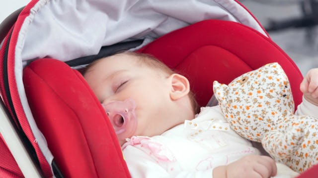 A baby sleeping in her stroller with a pacifier in her mouth while holding a toy