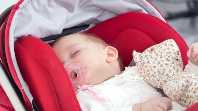 A baby sleeping in her stroller with a pacifier in her mouth while holding a toy 