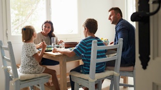 A man, sitting at a dining table eating breakfast with his wife and stepkids