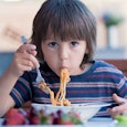 Little boy eating spaghetti for lunch, wearing a blue shirt with white and red stripes.