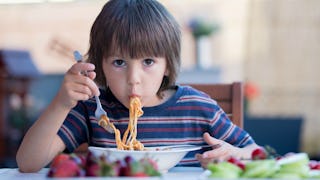 A boy in a striped blue-red shirt eating spaghetti in a restaurant