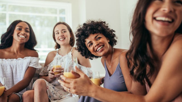 Four female friends at a get-together, sitting on a couch, smiling while having a drink