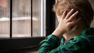 A ginger boy with CLOVES syndrome in a blue-green checked shirt holding his hand over his ear and lo...