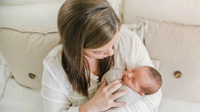 A mom holding her baby wrapped in a blanket, ready for breastfeeding.