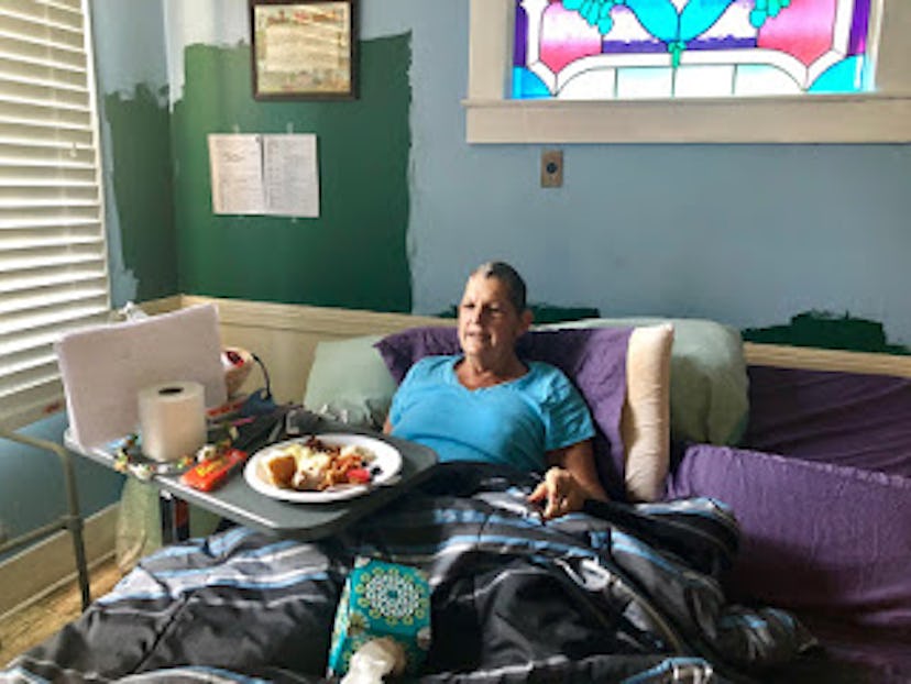 A woman sitting in a bedroom with a small table next to the bed with food on it