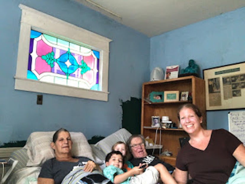 Grandparents, daughter, and children all together in a bedroom with blue walls