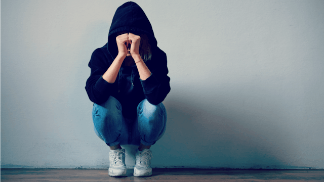 A desperate girl covering her face with her hands while leaned against the wall