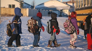 Kids entering a school bus during the winter, the snow has fallen.