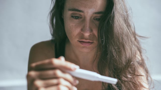 A woman holding a pregnancy test and looking sadly at it a she wants to keep it a secret from family...